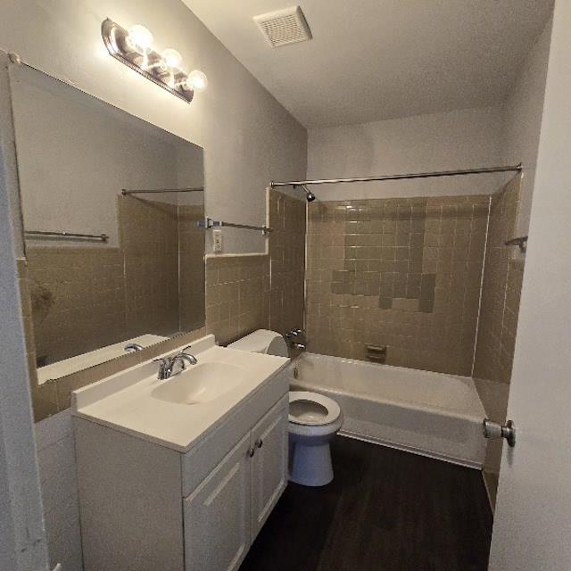 full bathroom with vanity, hardwood / wood-style flooring, tiled shower / bath combo, toilet, and tile walls