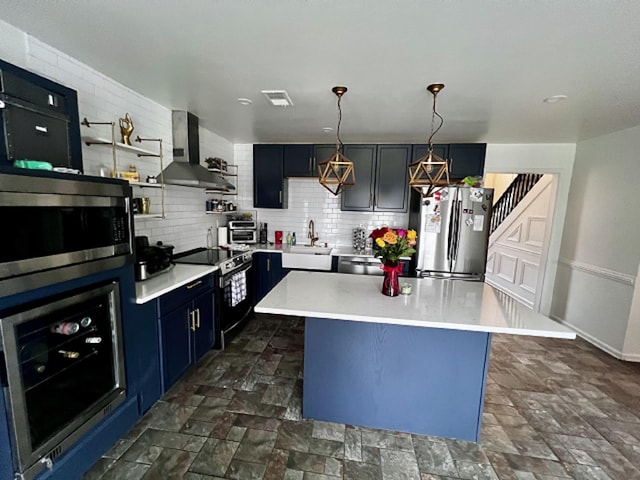 kitchen featuring appliances with stainless steel finishes, a center island, hanging light fixtures, and wall chimney range hood