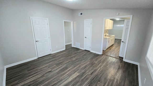 unfurnished bedroom featuring a textured ceiling, dark hardwood / wood-style floors, ensuite bathroom, and vaulted ceiling