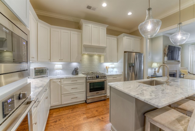 kitchen with sink, stainless steel appliances, tasteful backsplash, a center island with sink, and white cabinets