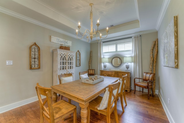 dining space featuring a tray ceiling, crown molding, dark wood-type flooring, and an inviting chandelier