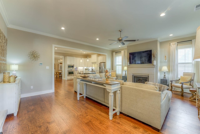 living room with wood-type flooring, plenty of natural light, ceiling fan, and ornamental molding