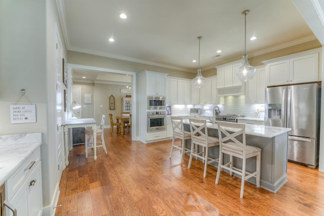 kitchen featuring light stone countertops, tasteful backsplash, stainless steel appliances, white cabinets, and an island with sink