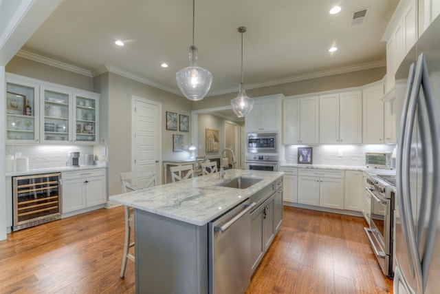 kitchen with white cabinetry, stainless steel appliances, tasteful backsplash, wine cooler, and a center island with sink