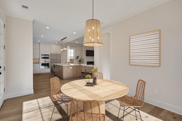 dining room featuring light hardwood / wood-style floors, crown molding, and sink