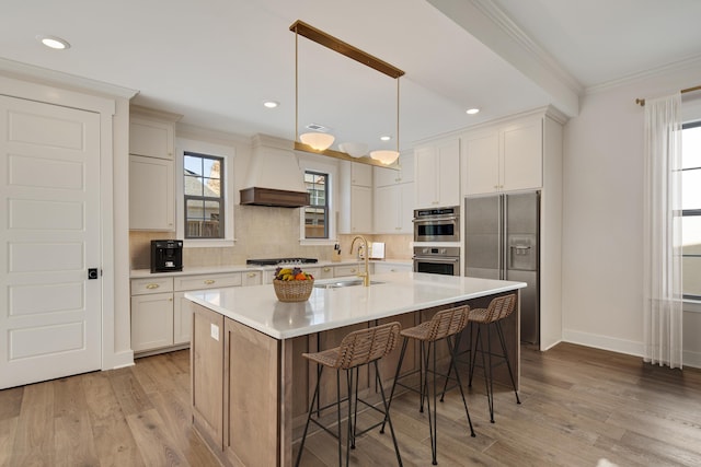 kitchen with backsplash, a kitchen island with sink, sink, appliances with stainless steel finishes, and custom range hood