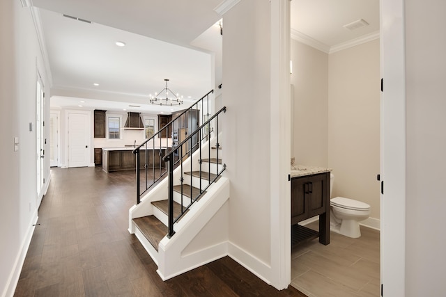 stairway with hardwood / wood-style floors, an inviting chandelier, and ornamental molding