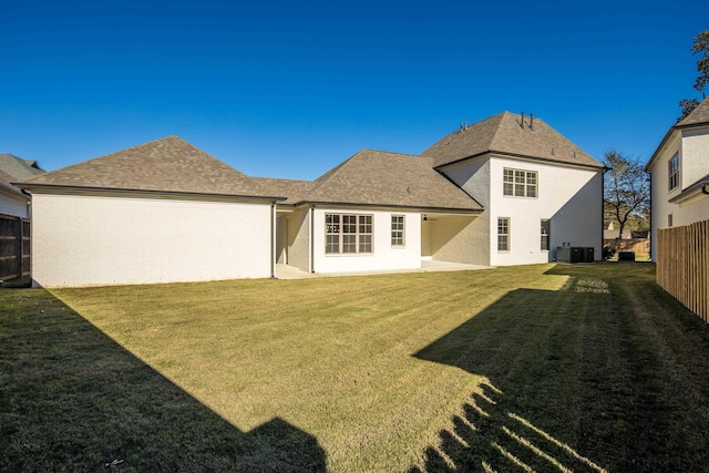 rear view of house with central AC unit and a yard