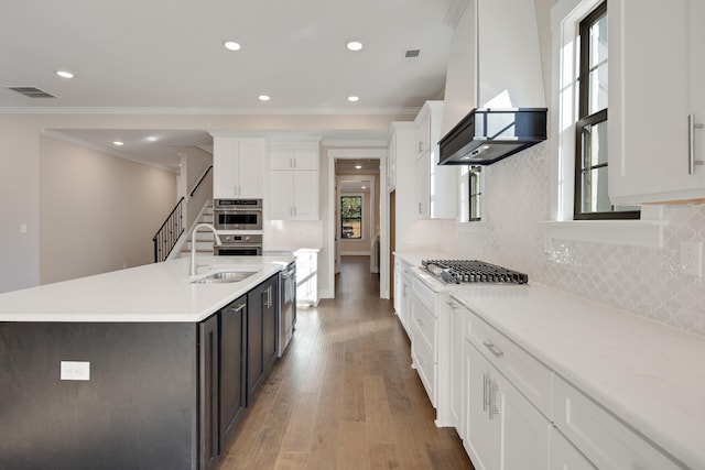 kitchen featuring backsplash, hardwood / wood-style floors, a center island with sink, white cabinets, and custom exhaust hood