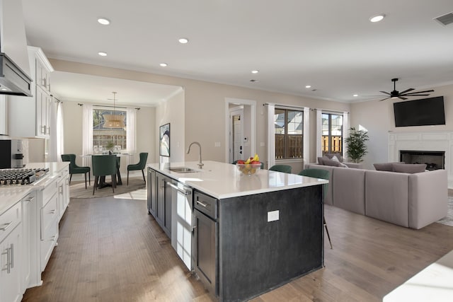 kitchen with a kitchen island with sink, sink, ceiling fan, light hardwood / wood-style floors, and white cabinetry