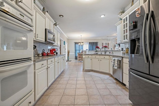 kitchen with light tile patterned flooring, appliances with stainless steel finishes, hanging light fixtures, ornamental molding, and kitchen peninsula