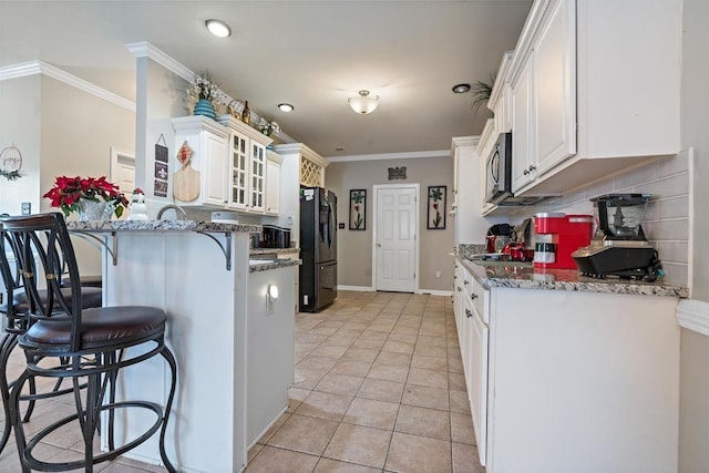 kitchen with light tile patterned floors, a breakfast bar, stone counters, black refrigerator, and white cabinets