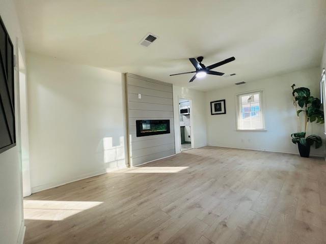 unfurnished living room with a fireplace, ceiling fan, and light hardwood / wood-style flooring