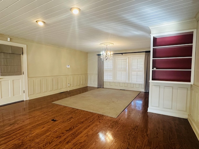 spare room featuring dark hardwood / wood-style floors, built in features, crown molding, and a chandelier