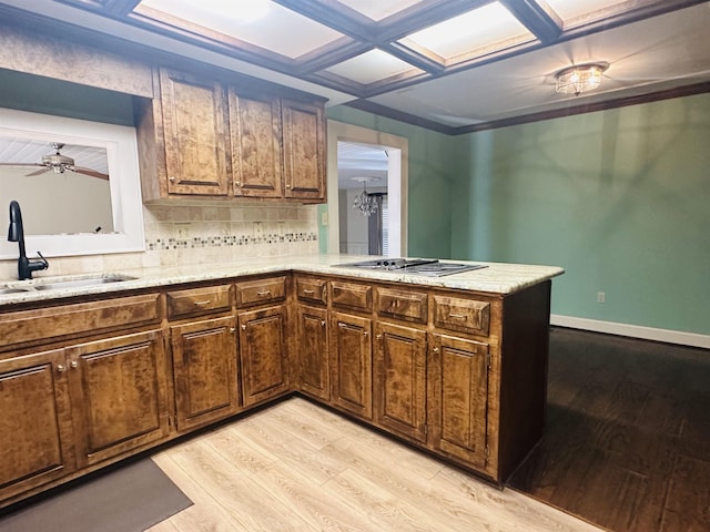 kitchen featuring stainless steel gas stovetop, sink, decorative backsplash, light wood-type flooring, and kitchen peninsula