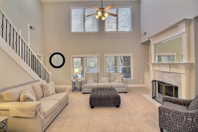 living room featuring light carpet, ceiling fan, a premium fireplace, and a high ceiling