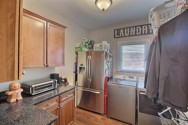 kitchen featuring stainless steel fridge with ice dispenser, washing machine and dryer, light hardwood / wood-style flooring, and dark stone countertops