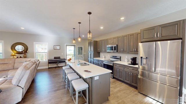 kitchen featuring a breakfast bar, hanging light fixtures, light hardwood / wood-style flooring, an island with sink, and appliances with stainless steel finishes