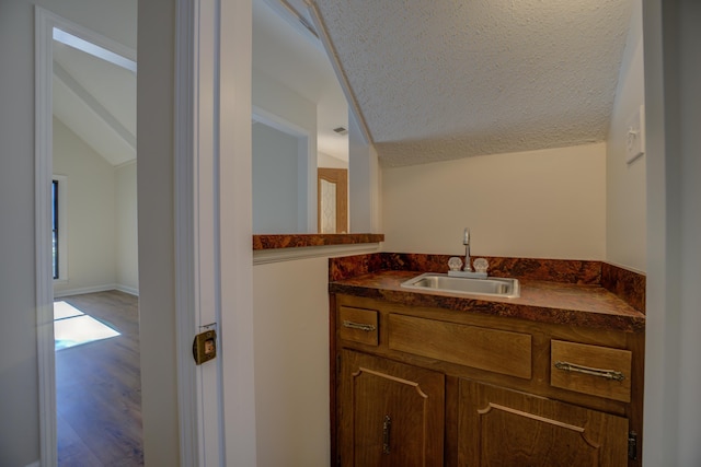 bathroom with vanity, a textured ceiling, hardwood / wood-style flooring, and vaulted ceiling