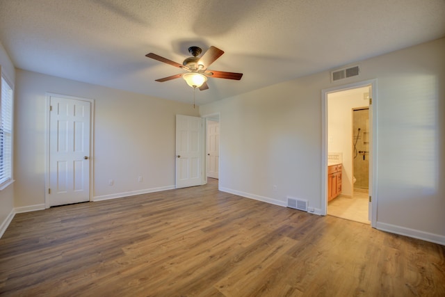 unfurnished bedroom with wood-type flooring, connected bathroom, a textured ceiling, and ceiling fan