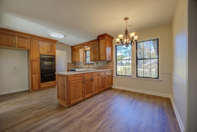 kitchen featuring decorative light fixtures, light hardwood / wood-style flooring, decorative backsplash, double oven, and a notable chandelier