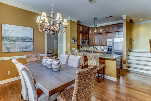 dining area with crown molding, light wood-type flooring, and a notable chandelier