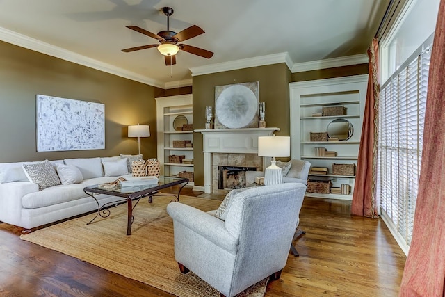 living room with a tiled fireplace, crown molding, ceiling fan, and light wood-type flooring