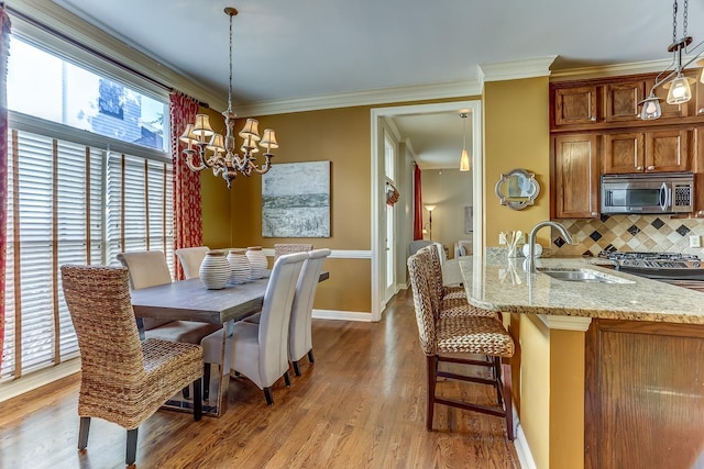 dining space with crown molding, sink, light hardwood / wood-style floors, and an inviting chandelier