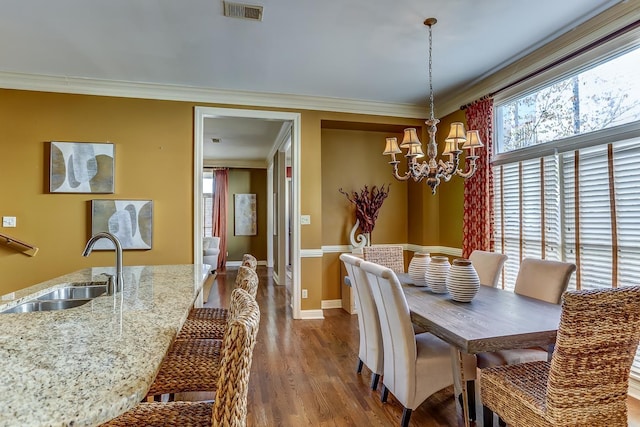 dining area featuring sink, hardwood / wood-style floors, a notable chandelier, and ornamental molding