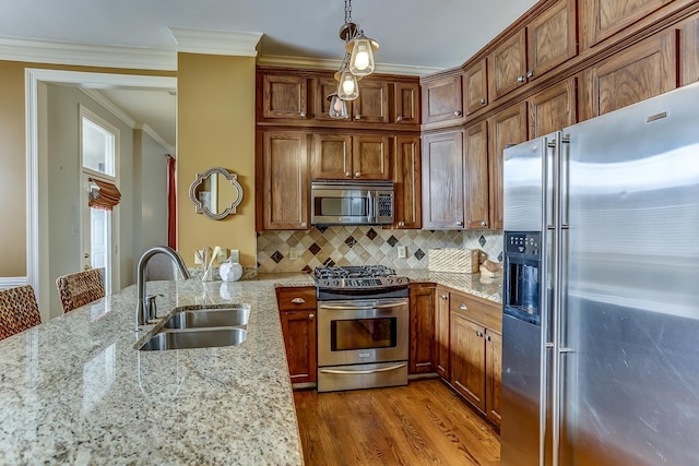 kitchen featuring light stone counters, ornamental molding, stainless steel appliances, sink, and hanging light fixtures