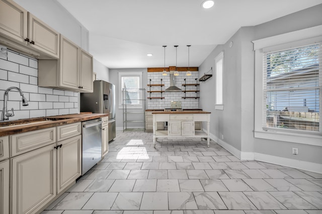 kitchen with wooden counters, appliances with stainless steel finishes, extractor fan, sink, and hanging light fixtures