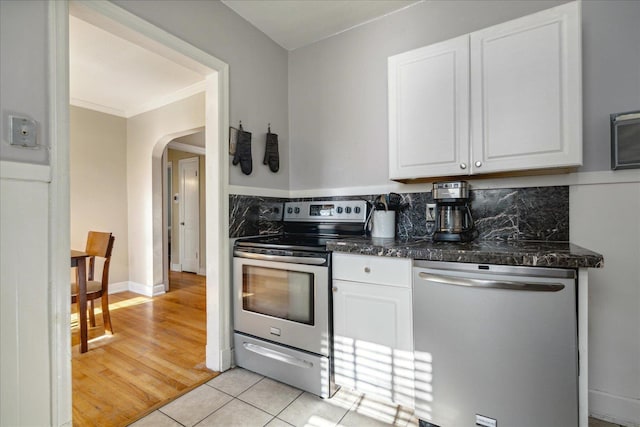 kitchen featuring backsplash, dark stone counters, stainless steel appliances, light tile patterned floors, and white cabinets