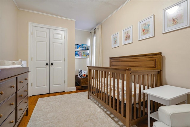 bedroom featuring a closet, a nursery area, light wood-type flooring, and ornamental molding