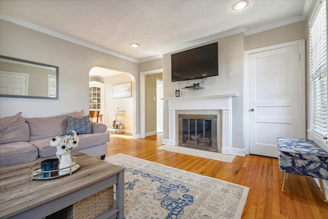 living room with light hardwood / wood-style floors, ornamental molding, a textured ceiling, and a tiled fireplace