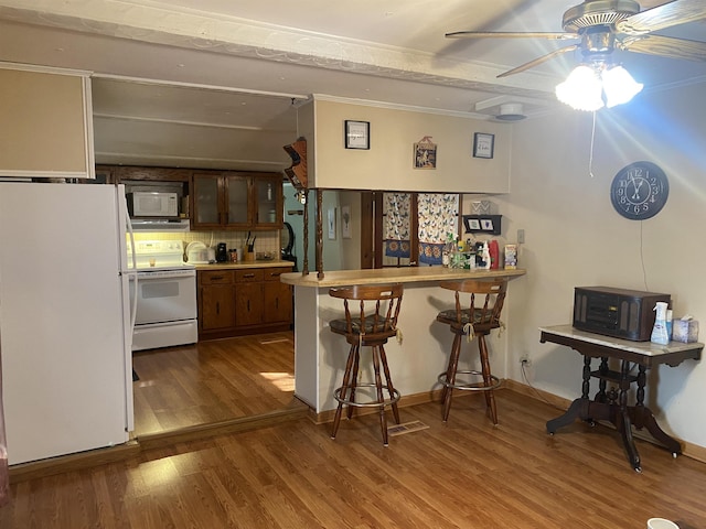 kitchen with a breakfast bar, white appliances, dark wood-type flooring, ceiling fan, and kitchen peninsula