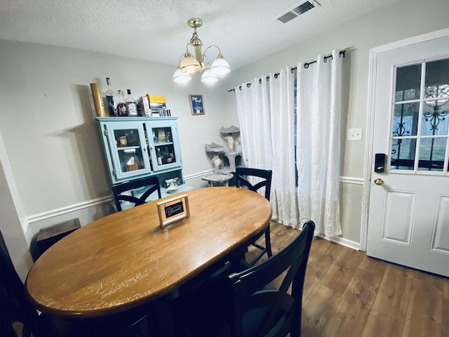 dining space with a chandelier, dark wood-type flooring, and a textured ceiling