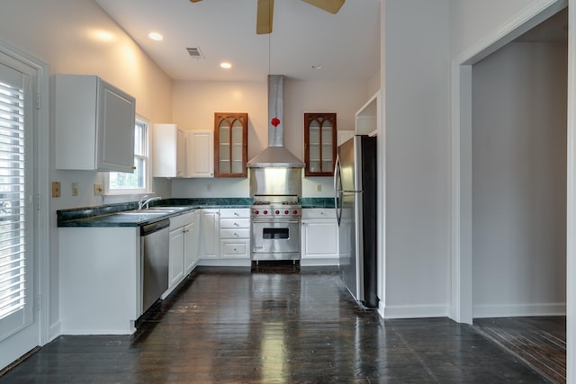 kitchen with sink, dark wood-type flooring, stainless steel appliances, wall chimney range hood, and white cabinets