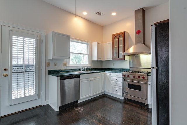 kitchen featuring dark wood-type flooring, white cabinets, wall chimney range hood, sink, and stainless steel appliances