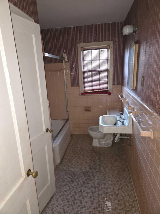 full bathroom featuring toilet, shower / bath combination with glass door, sink, and tile walls