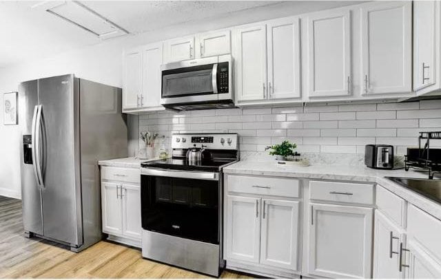 kitchen with decorative backsplash, white cabinetry, light hardwood / wood-style flooring, and stainless steel appliances