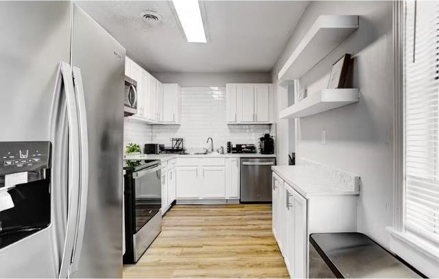 kitchen with tasteful backsplash, white cabinetry, light hardwood / wood-style flooring, and appliances with stainless steel finishes