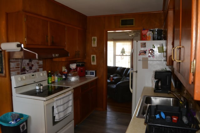 kitchen with sink, white appliances, wooden walls, dark hardwood / wood-style floors, and exhaust hood