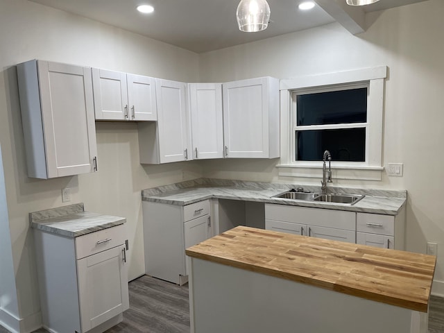 kitchen featuring white cabinetry, sink, hanging light fixtures, wood counters, and wood-type flooring