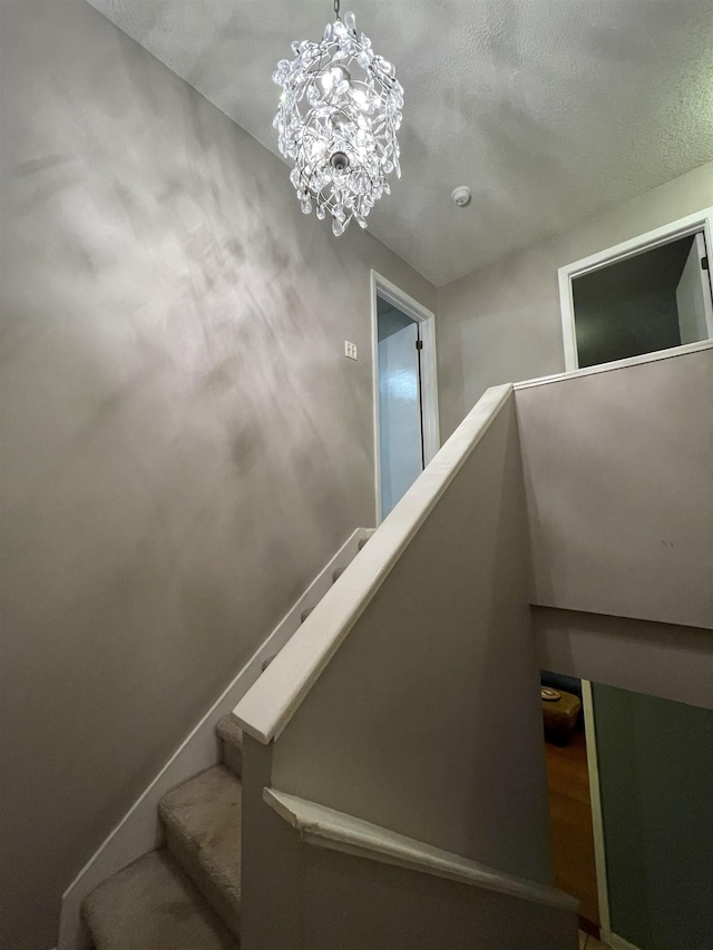 stairs with a textured ceiling and an inviting chandelier