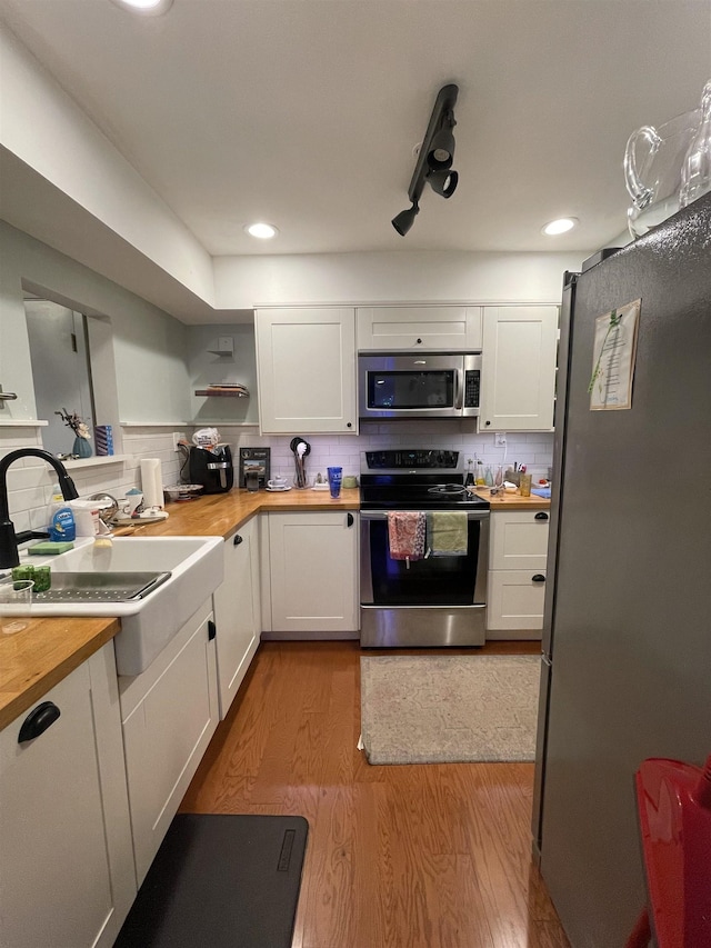 kitchen featuring white cabinetry, wood counters, tasteful backsplash, appliances with stainless steel finishes, and light wood-type flooring