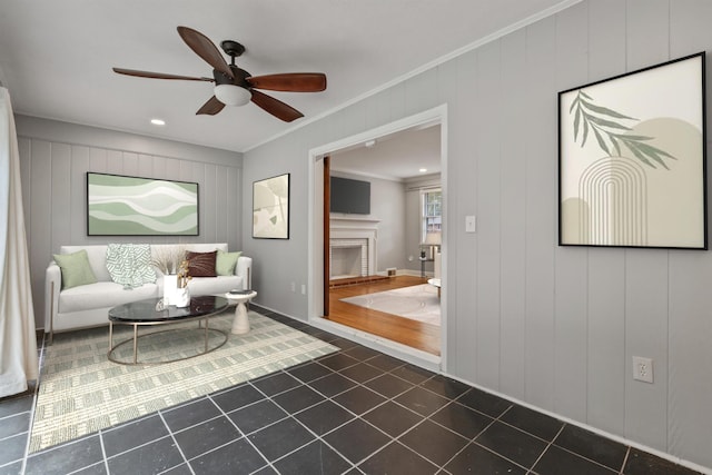 tiled living room with ceiling fan, wooden walls, and ornamental molding