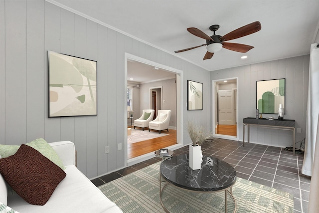 living room with ceiling fan, dark tile patterned floors, crown molding, and wood walls