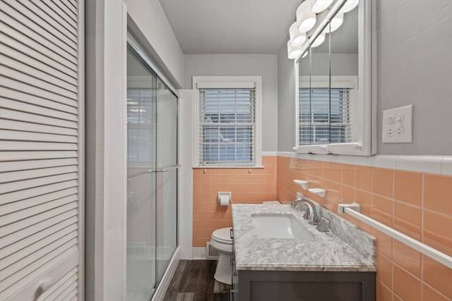 bathroom featuring vanity, hardwood / wood-style flooring, toilet, tile walls, and a shower with shower door