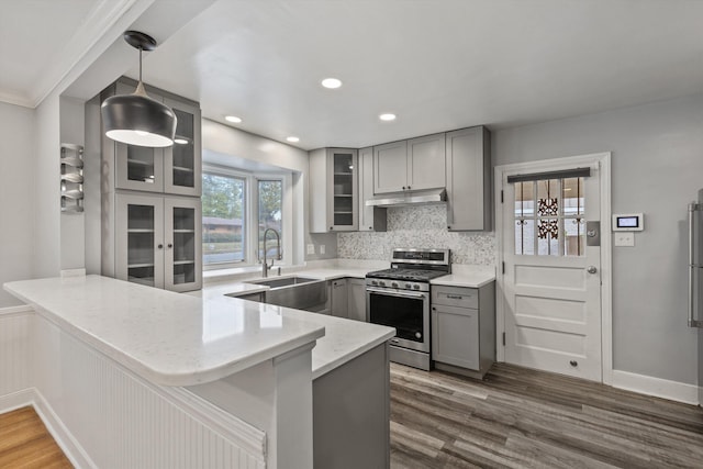 kitchen featuring sink, dark wood-type flooring, stainless steel range with gas cooktop, kitchen peninsula, and pendant lighting