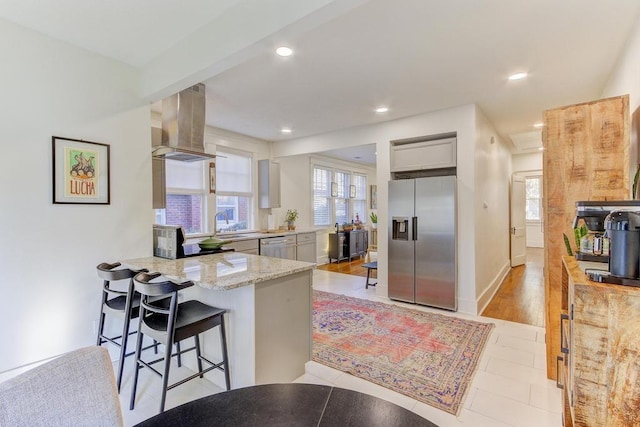 kitchen featuring stainless steel appliances, light hardwood / wood-style flooring, gray cabinets, a breakfast bar area, and range hood